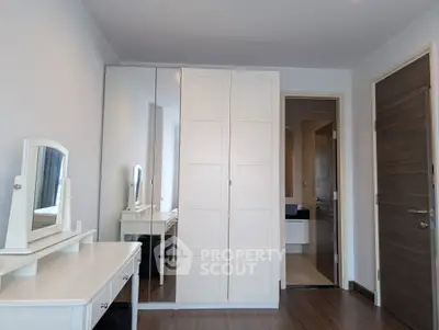 Spacious bedroom with elegant white wardrobe and vanity set, featuring sleek wooden flooring.