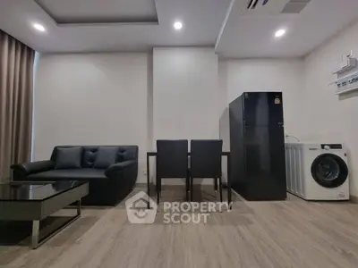 Modern living room with sleek furniture, black sofa, dining set, fridge, and washing machine.
