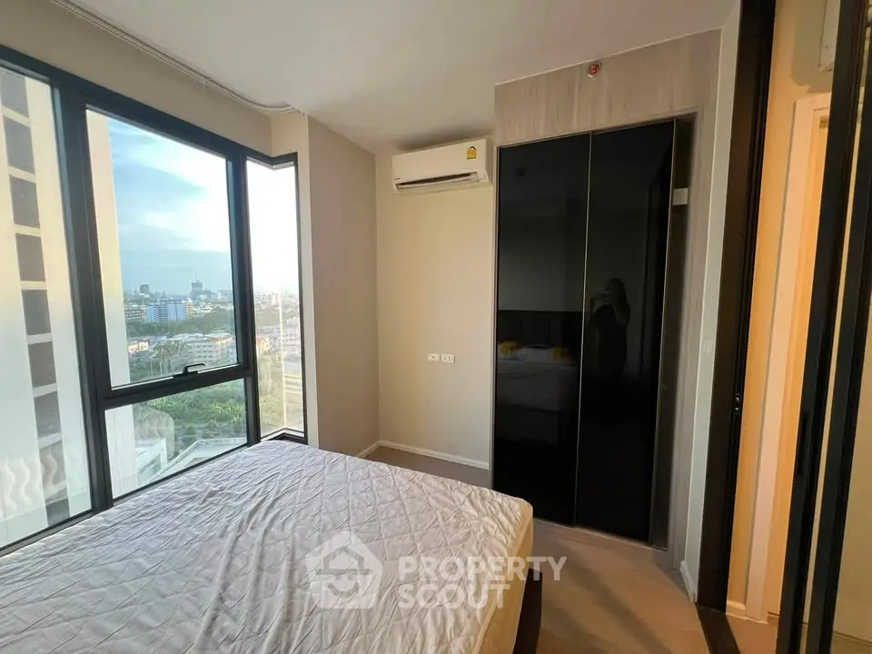 Modern bedroom with large windows and city view, featuring a sleek wardrobe and air conditioning unit.