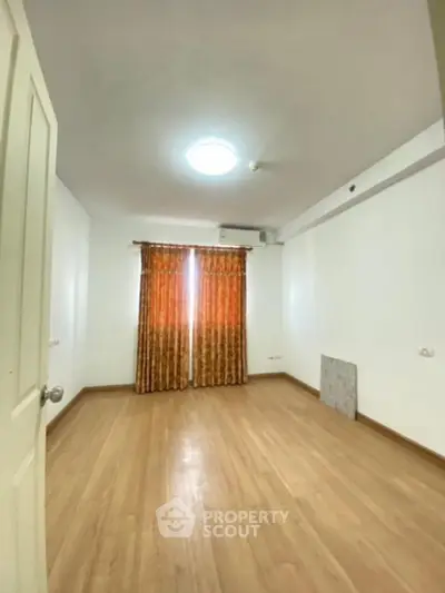 Spacious and well-lit living room with polished wooden flooring and vibrant orange curtains, perfect for a cozy family gathering space.