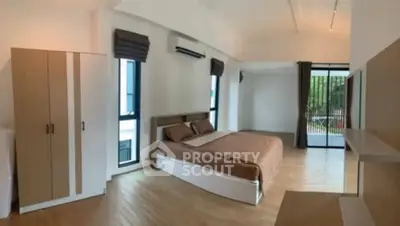 Spacious modern bedroom with large windows and balcony access, featuring sleek wooden flooring.