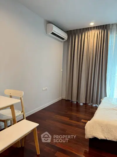 Cozy bedroom with wooden flooring and air conditioning, featuring a small dining area.