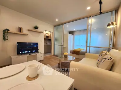 Modern living room with cozy sofa, TV, and open layout leading to a bedroom with glass partition.