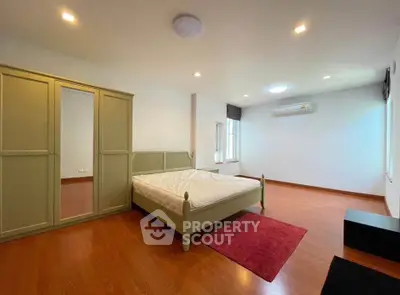 Spacious bedroom with wooden flooring and modern furnishings in a bright, airy setting.