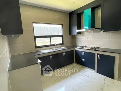Modern kitchen with sleek cabinetry and gas stove, featuring a bright window and marble flooring.