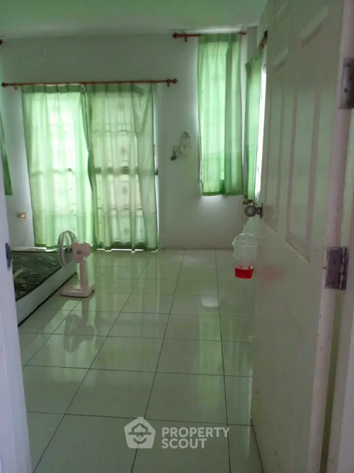 Spacious bedroom with green curtains and tiled floor, offering a serene atmosphere.