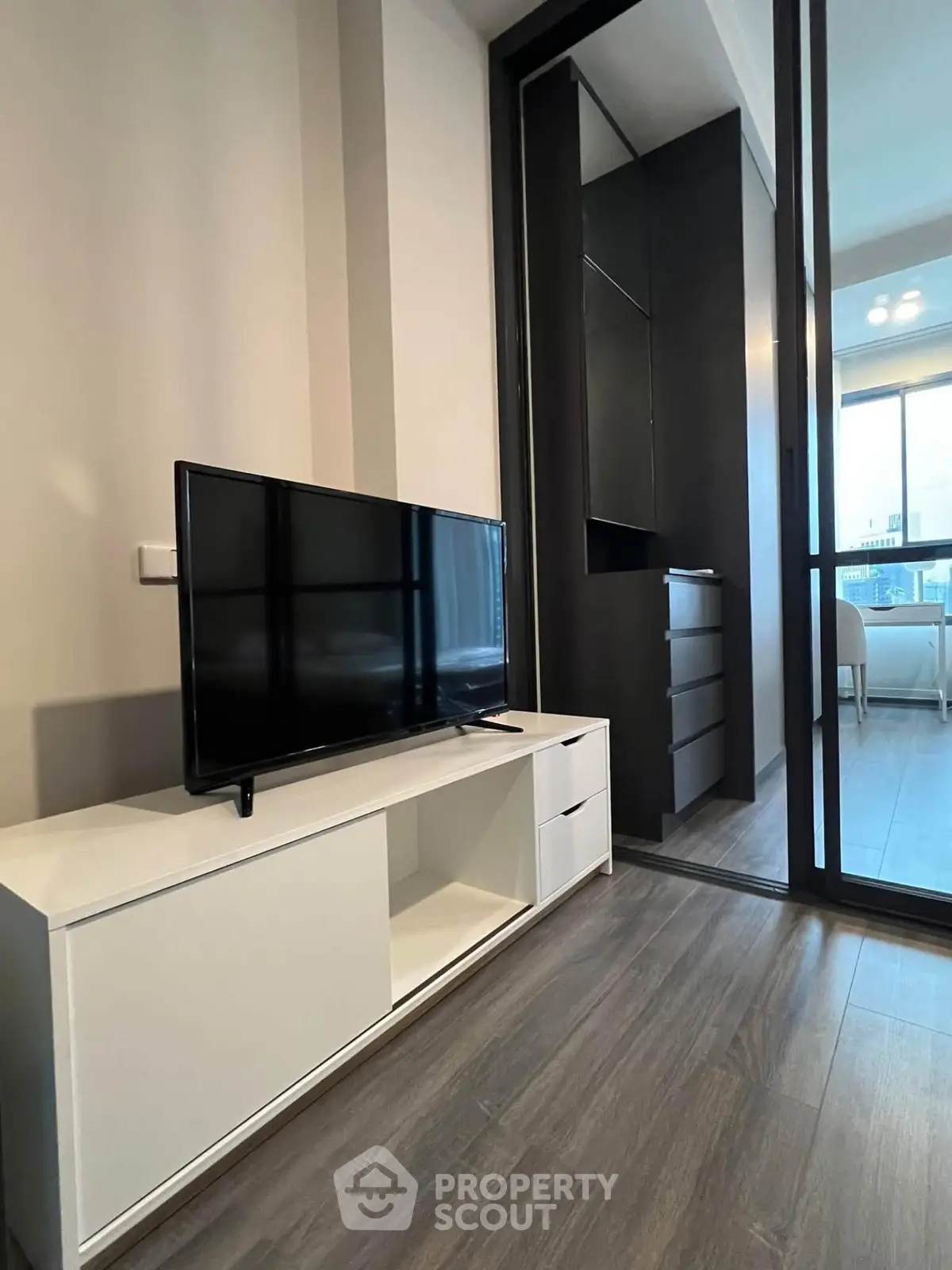 Modern living room with sleek TV stand and sliding glass door leading to a bright balcony.