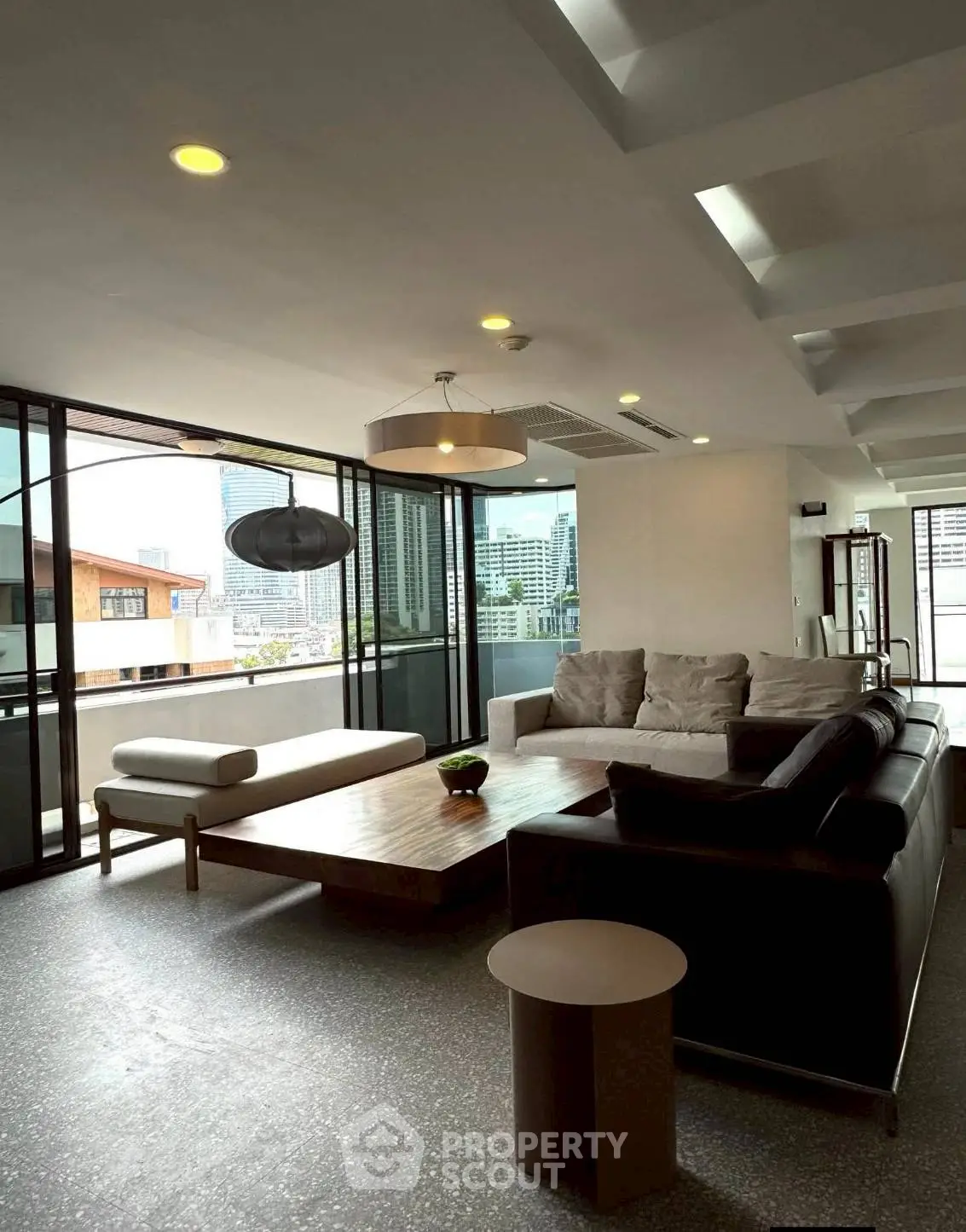Spacious modern living room with large windows and city view, featuring stylish furniture and contemporary lighting.