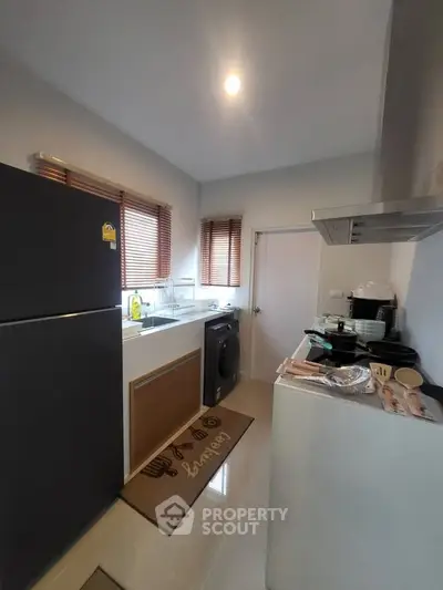 Modern kitchen with sleek appliances and ample natural light, featuring a washing machine and large refrigerator.