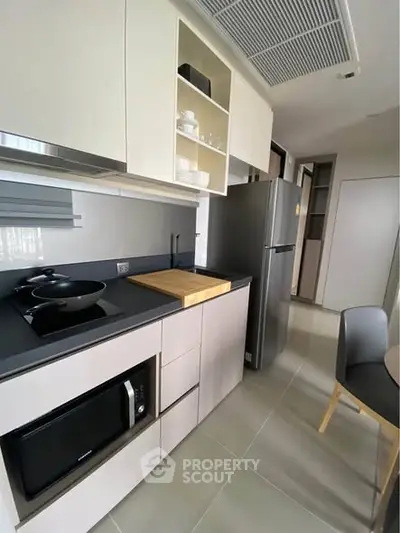 Modern kitchen with sleek cabinetry, built-in microwave, and stainless steel fridge in a compact layout.