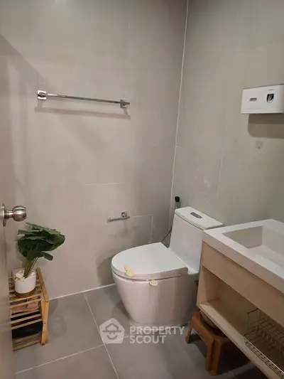 Modern bathroom with sleek fixtures and minimalist design, featuring a toilet, sink, and decorative plant.