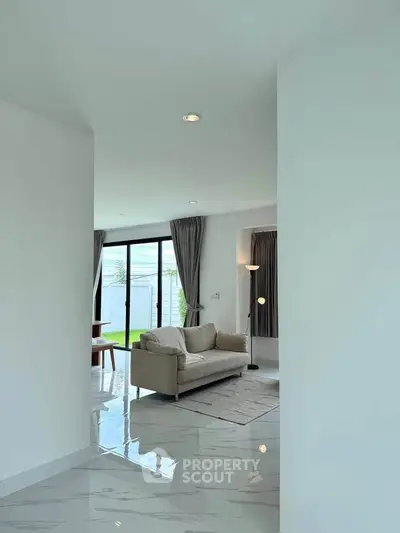 Modern living room with sleek sofa and large windows opening to a garden view, featuring elegant curtains and polished floors.