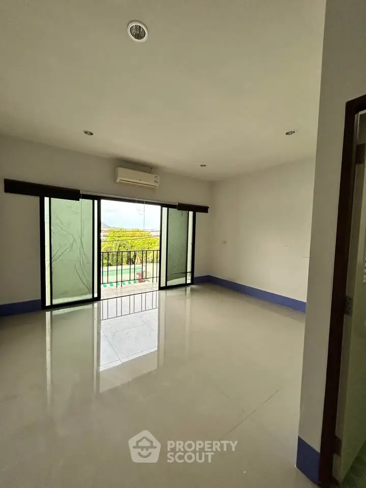 Spacious empty room with balcony and large windows offering natural light and outdoor view.