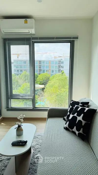 Chic living room with modern decor and large window offering a scenic view of greenery and buildings.