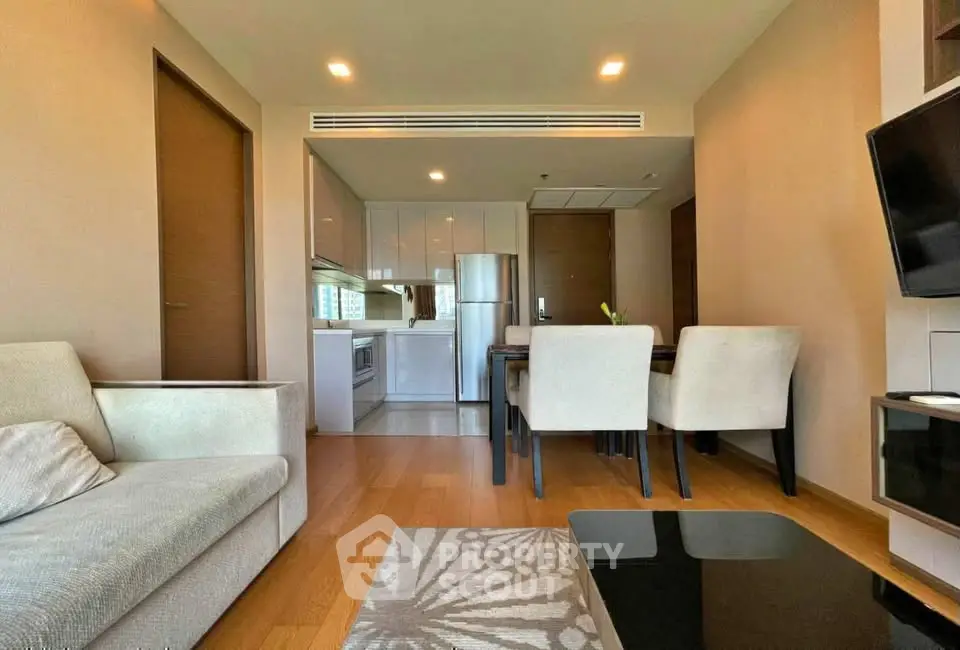 Modern living room with open kitchen and dining area, featuring sleek furniture and wooden flooring.