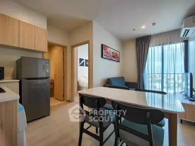 Modern living room with open kitchen, stylish furniture, and natural light from large window.