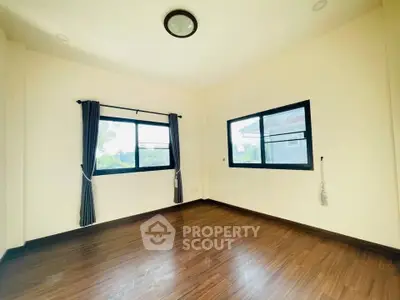 Spacious empty room with wooden flooring and large windows offering natural light.