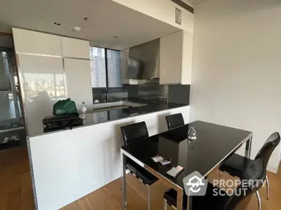 Modern kitchen with sleek black countertops and high-gloss cabinetry, complemented by a stylish dining area with a contemporary table set.