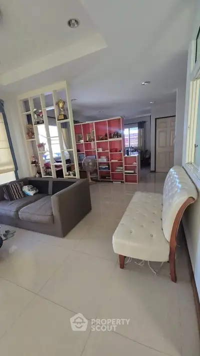 Spacious living room with modern decor and ample natural light, featuring a cozy sofa and stylish shelving.
