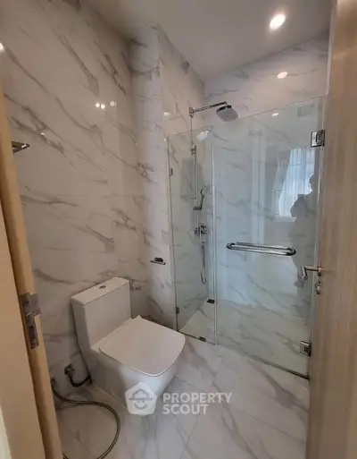 Modern bathroom with marble tiles and glass shower enclosure in a luxury apartment.