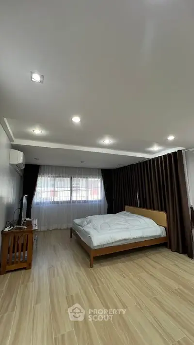 Spacious bedroom with modern lighting and large window, featuring wooden flooring and elegant curtains.