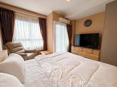 Cozy bedroom with modern decor, featuring a large TV and comfortable seating area.