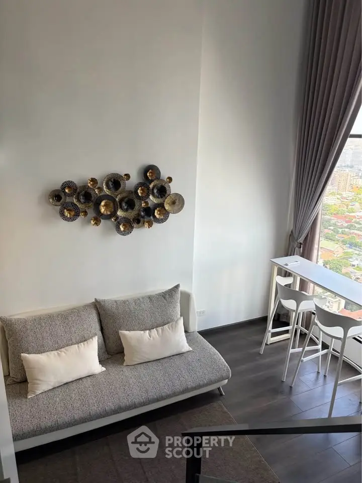 Modern living room with high ceiling and city view, featuring stylish decor and floor-to-ceiling windows.