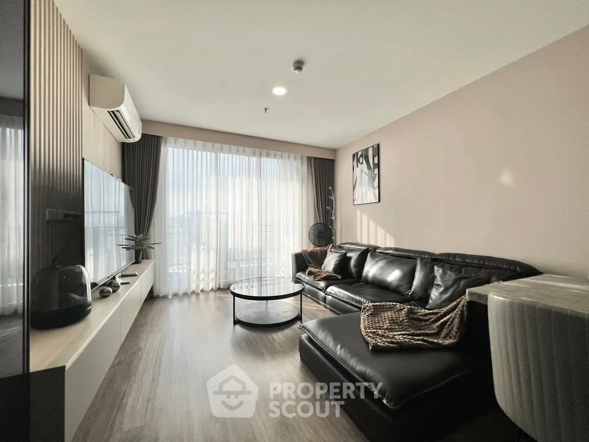 Modern living room with sleek black leather sofa and large window, offering ample natural light.