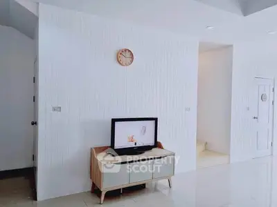 Modern minimalist living room with sleek TV stand and wall clock, featuring bright white decor.