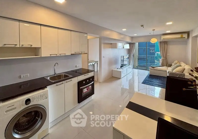 Modern open-plan living room with sleek kitchen and city view balcony.