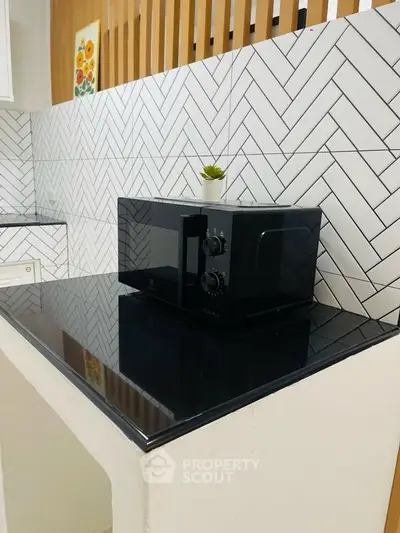 Modern kitchen with sleek black microwave and stylish herringbone backsplash.