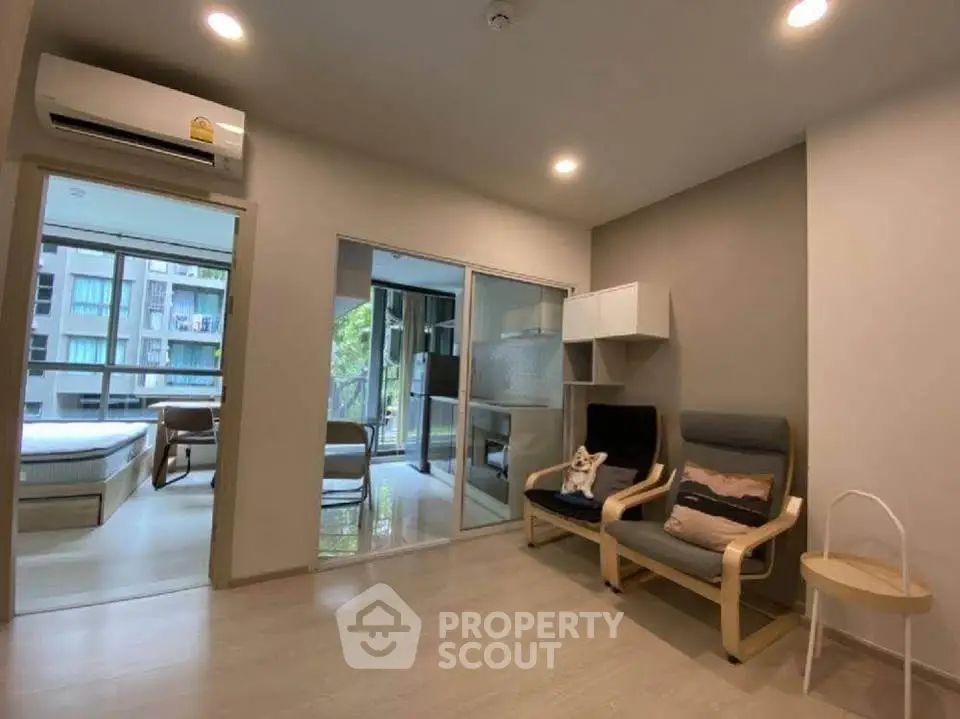 Modern living room with cozy seating and view into a bright bedroom, featuring sleek design and ample natural light.