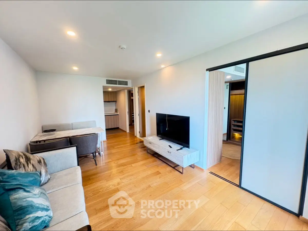 Modern living room with wooden flooring, stylish furniture, and sliding door to kitchen.