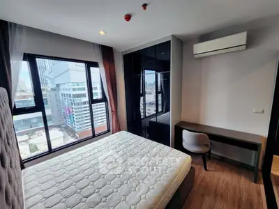 Modern bedroom with city view, featuring large windows and sleek furniture.