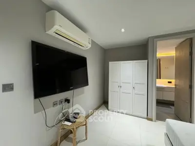 Modern bedroom with wall-mounted TV and air conditioning unit, featuring sleek wardrobe and minimalist decor.
