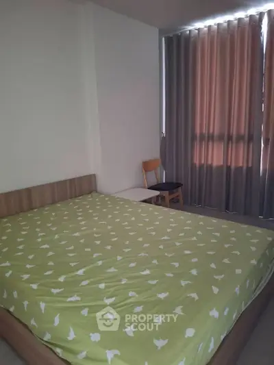 Cozy bedroom with green bedspread and natural light through curtains.