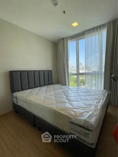 Modern bedroom with large window offering city view, featuring a comfortable bed and stylish decor.