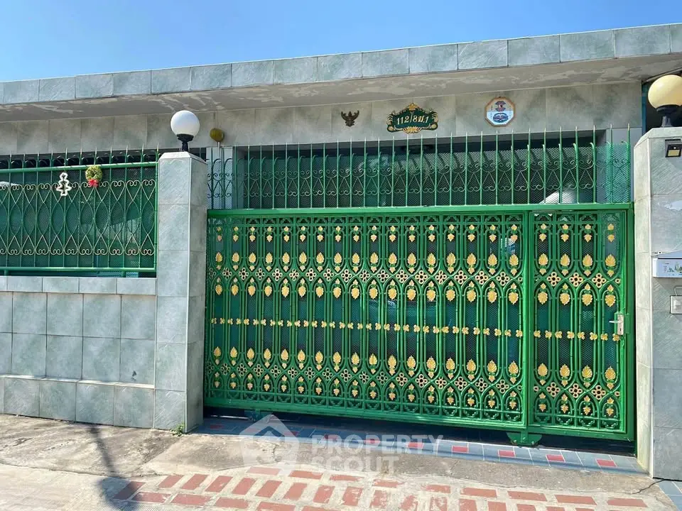 Charming house exterior with ornate green gate and tiled facade under clear blue sky.