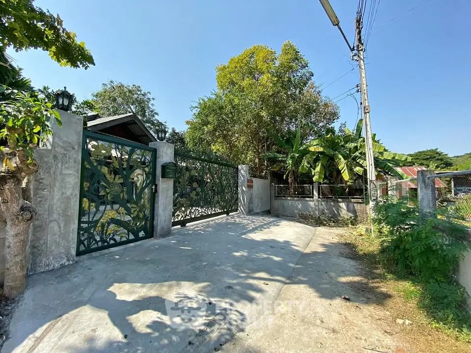 Charming gated entrance with lush greenery and concrete driveway