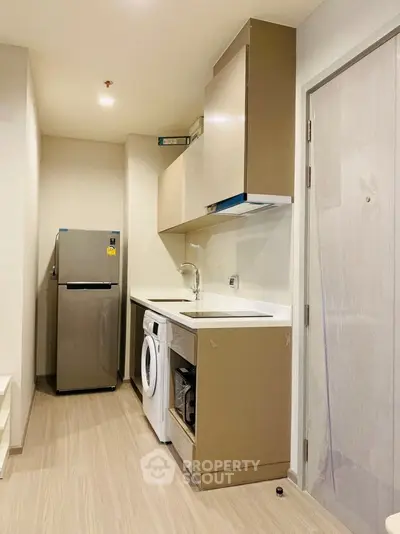 Modern compact kitchen with washing machine and fridge in sleek apartment.