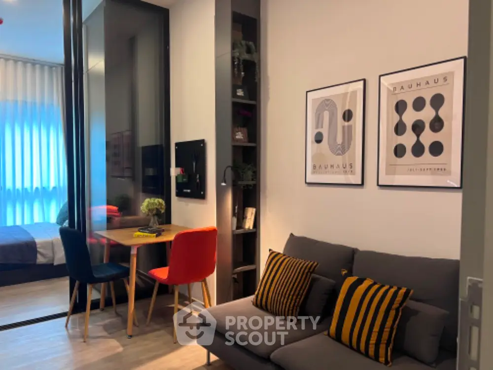 Modern living room with stylish decor, cozy seating, and a small dining area, adjacent to a bedroom with natural light.