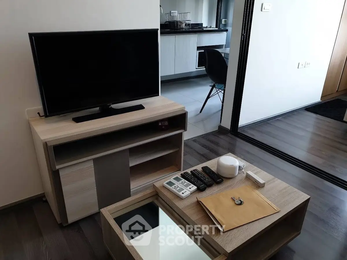 Modern living room with sleek TV stand and coffee table, open layout to kitchen area.