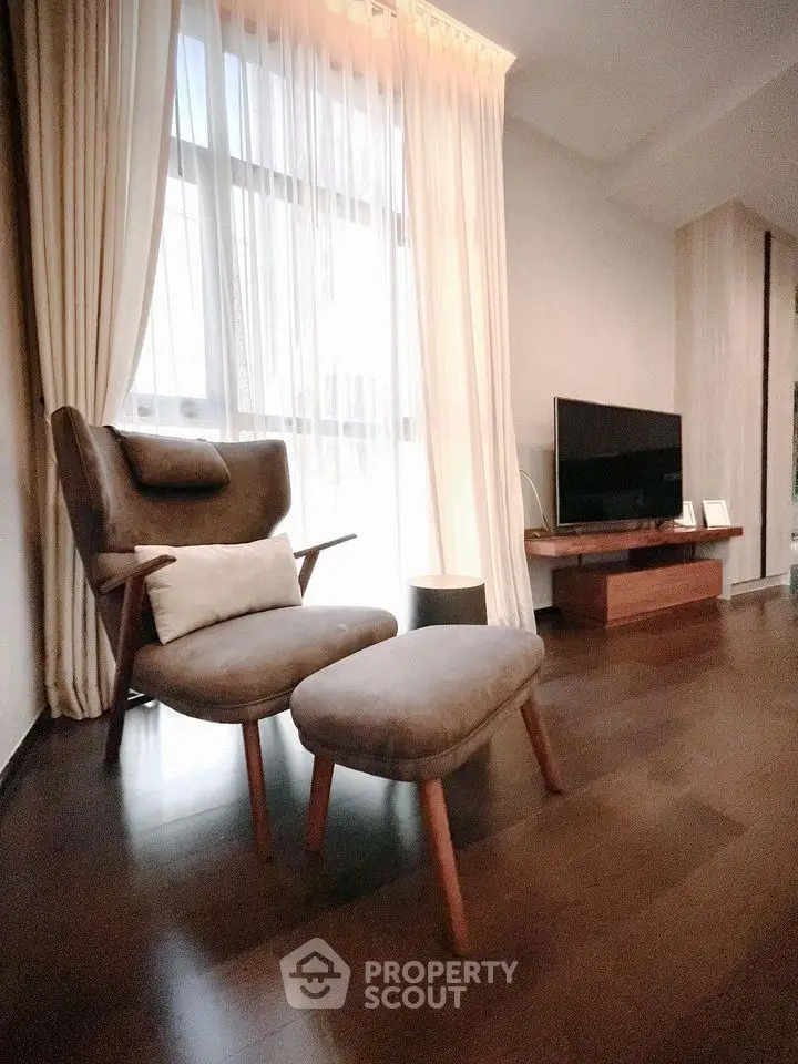 Elegant living room with cozy armchair, ottoman, and modern TV setup, featuring warm lighting and stylish decor.