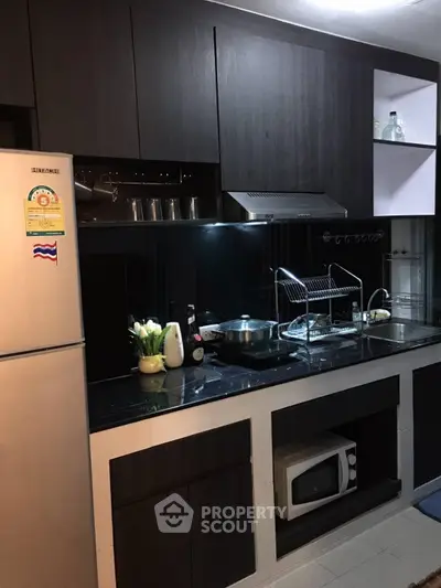 Modern kitchen with sleek black cabinetry and stainless steel appliances, featuring a microwave and elegant decor.
