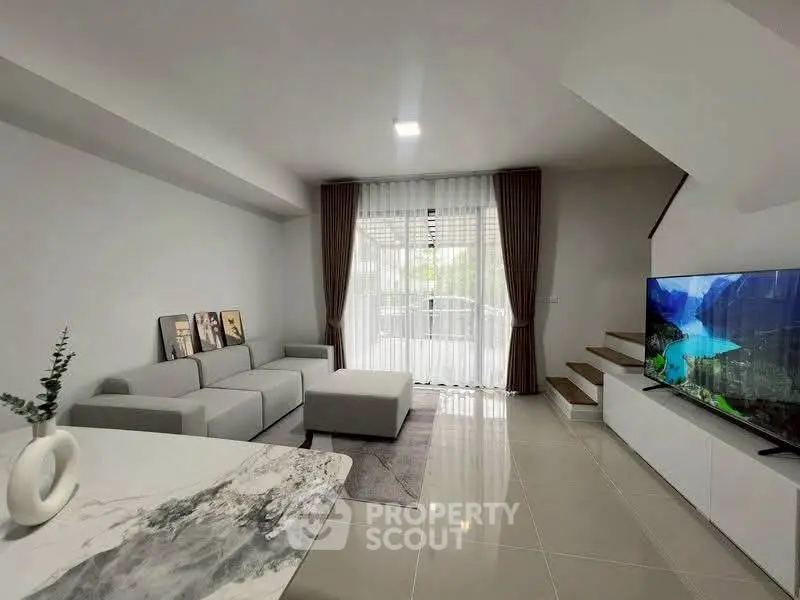 Modern living room with sleek furniture and large window offering natural light.