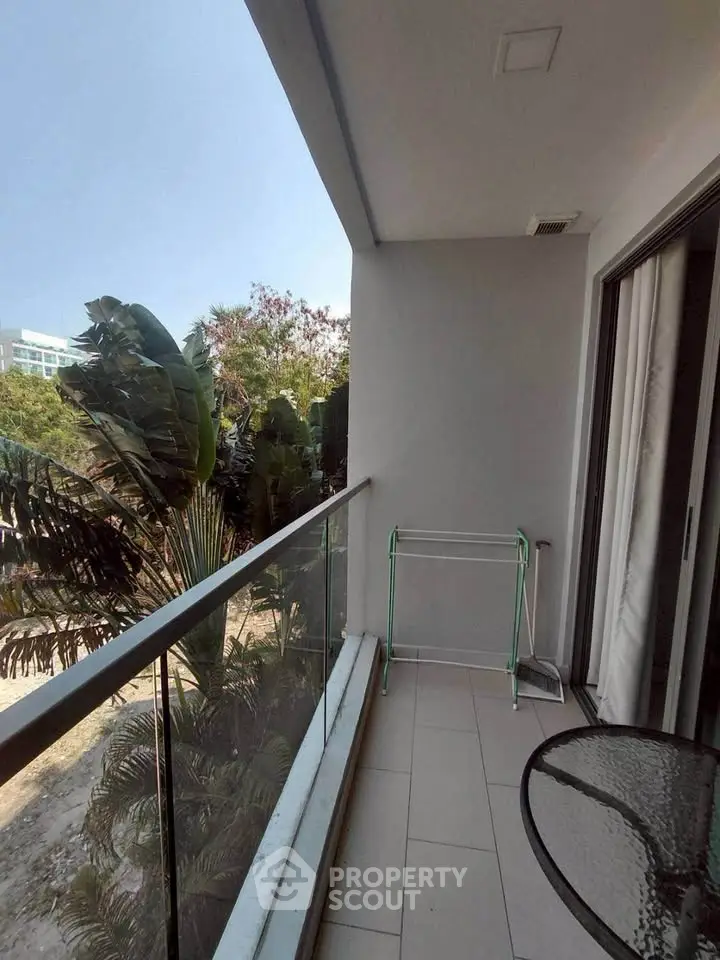 Spacious balcony with glass railing and lush greenery view, perfect for relaxation and outdoor dining.