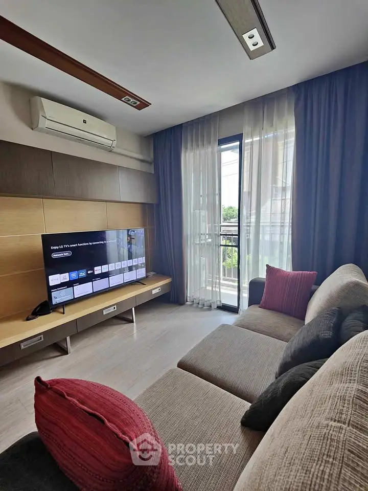 Modern living room with large TV and cozy sofa, featuring elegant curtains and air conditioning.
