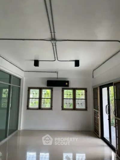 Spacious room with large windows and modern lighting, ideal for versatile living space.
