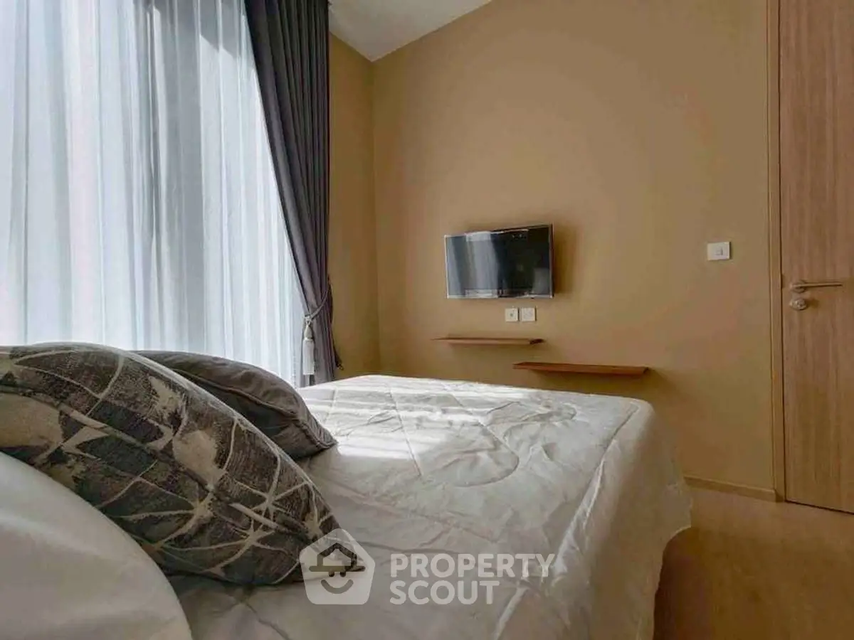 Cozy bedroom with modern decor and wall-mounted TV, featuring large windows and elegant curtains.