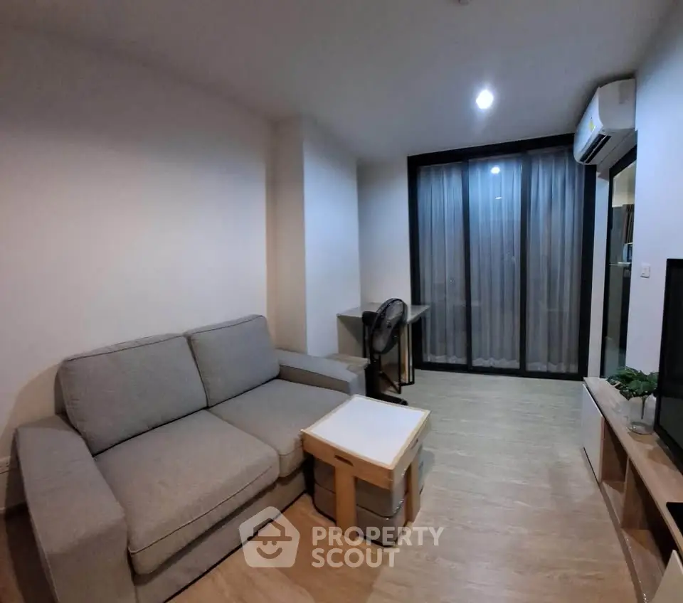 Modern living room with cozy gray sofa, sleek TV stand, and large window with curtains.